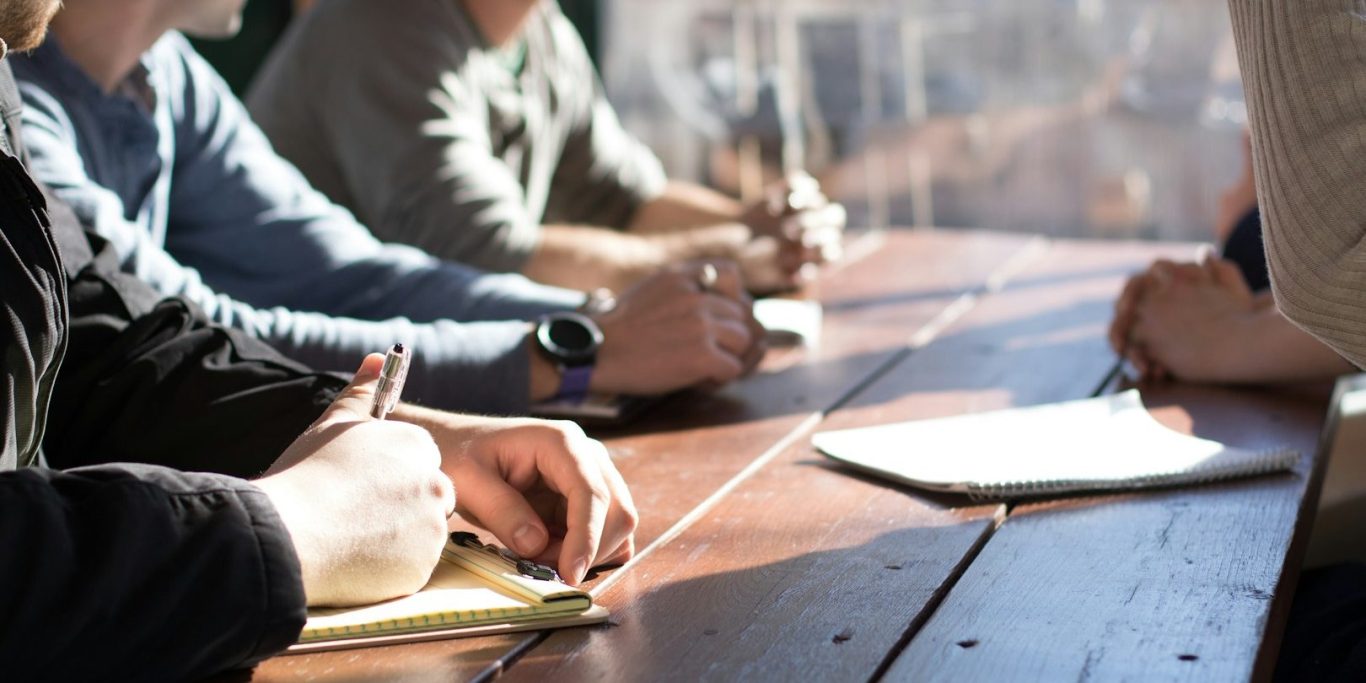 Interactive HR & Leadership Training Hands of several people taking notes at a wooden table during a meeting.