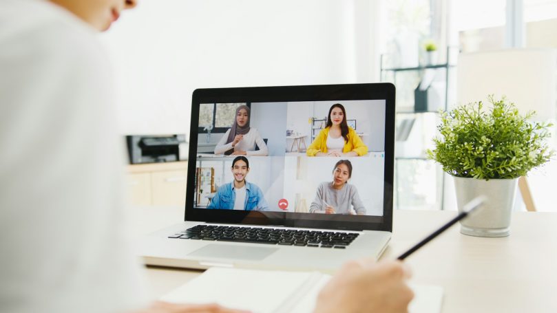 Remote Person taking notes during a video conference with four participants on a laptop screen.